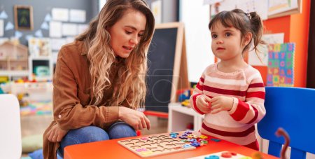 Foto de Maestro y niño pequeño jugando con las matemáticas juego de puzzle sentado en la mesa en el jardín de infantes - Imagen libre de derechos