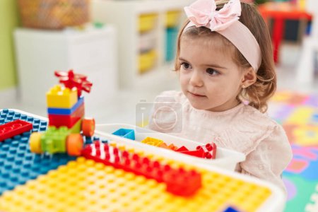 Foto de Adorable niño rubio jugando con bloques de construcción sentado en la mesa en el jardín de infantes - Imagen libre de derechos