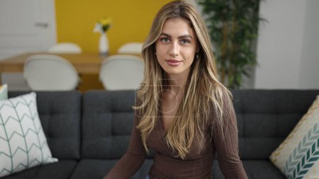 Foto de Young blonde woman sitting on sofa with relaxed expression at home - Imagen libre de derechos