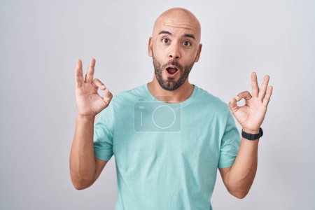 Photo for Middle age bald man standing over white background looking surprised and shocked doing ok approval symbol with fingers. crazy expression - Royalty Free Image