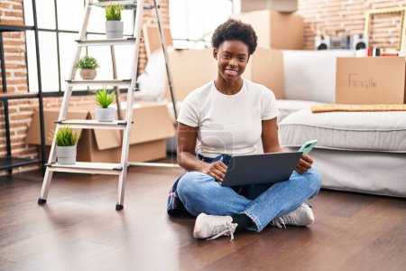 Téléchargez les photos : African american woman using laptop and smartphone sitting on floor at new home - en image libre de droit