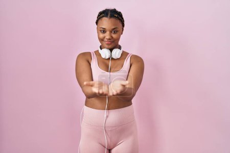 Photo for African american woman with braids wearing sportswear and headphones smiling with hands palms together receiving or giving gesture. hold and protection - Royalty Free Image