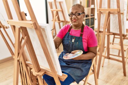 Foto de Mujer afroamericana mayor sonriendo dibujo confiado en el estudio de arte - Imagen libre de derechos