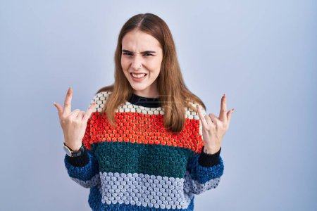 Photo for Young hispanic girl standing over blue background shouting with crazy expression doing rock symbol with hands up. music star. heavy music concept. - Royalty Free Image