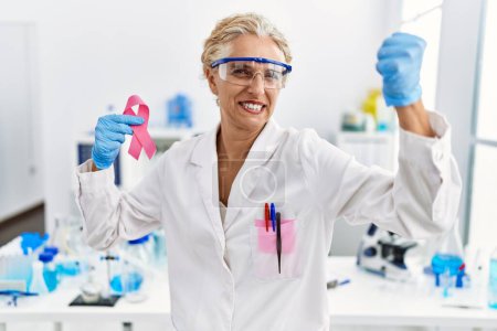 Photo for Middle age blonde woman working at laboratory looking for breast cancer cure annoyed and frustrated shouting with anger, yelling crazy with anger and hand raised - Royalty Free Image