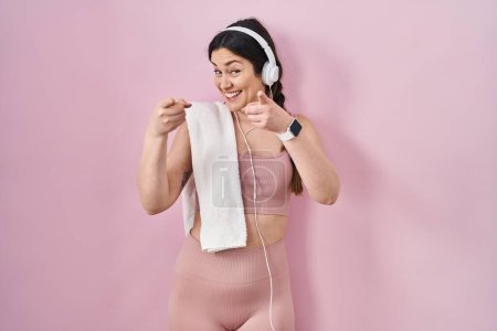 Foto de Young brunette woman wearing sportswear and headphones pointing fingers to camera with happy and funny face. good energy and vibes. - Imagen libre de derechos