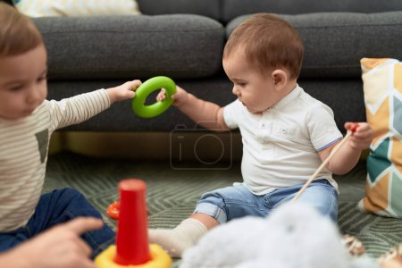 Foto de Dos niños adorables jugando con juguetes sentados en el suelo en casa - Imagen libre de derechos