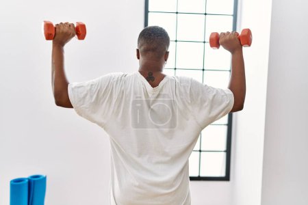 Téléchargez les photos : Jeune homme africain s'entraînant avec des haltères à la salle de gym - en image libre de droit