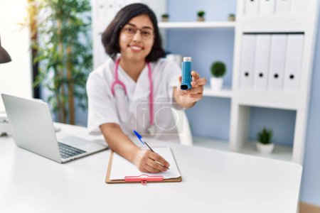 Téléchargez les photos : Jeune femme latine portant l'uniforme de médecin tenant inhalateur écriture sur presse-papiers à la clinique - en image libre de droit