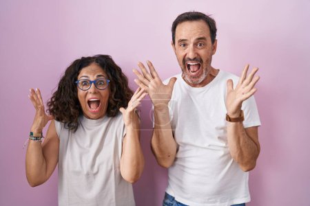 Téléchargez les photos : Middle age hispanic couple together over pink background celebrating crazy and amazed for success with arms raised and open eyes screaming excited. winner concept - en image libre de droit