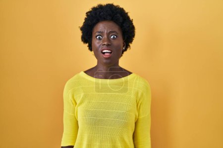 Téléchargez les photos : Jeune femme africaine debout sur jaune studio en colère et fou hurlant frustré et furieux, criant de colère. rage et concept agressif. - en image libre de droit