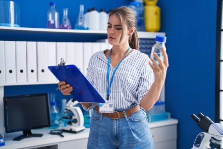 Photo for Young woman scientist reading document holding bottle at laboratory - Royalty Free Image