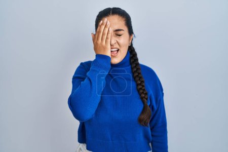 Foto de Young hispanic woman standing over isolated background yawning tired covering half face, eye and mouth with hand. face hurts in pain. - Imagen libre de derechos