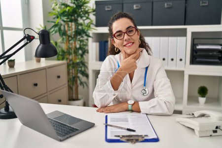 Photo for Young hispanic woman wearing doctor uniform and stethoscope looking confident at the camera smiling with crossed arms and hand raised on chin. thinking positive. - Royalty Free Image