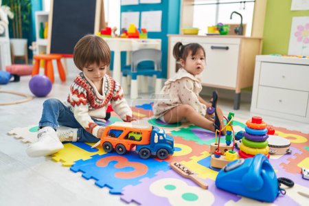 Foto de Two kids playing with cars toy sitting on floor at kindergarten - Imagen libre de derechos
