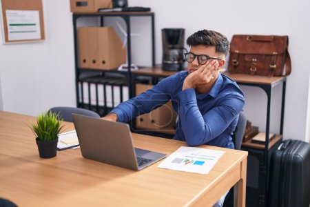 Téléchargez les photos : Jeune homme hispanique travailleur d'affaires utilisant un ordinateur portable avec une expression sérieuse au bureau - en image libre de droit