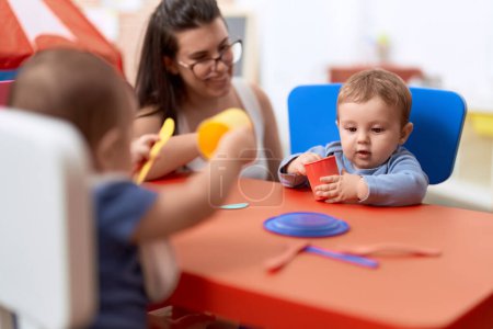 Foto de Profesor y estudiante de preescolar sentado en la mesa aprendiendo a comer en el jardín de infantes - Imagen libre de derechos