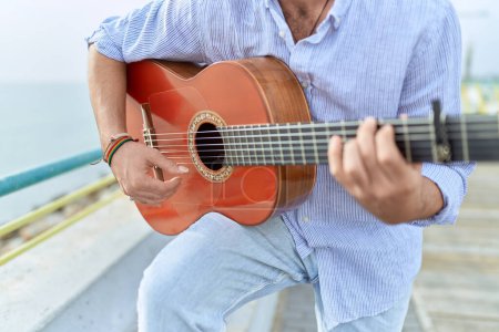 Téléchargez les photos : Young hispanic man musician playing classical guitar at seaside - en image libre de droit