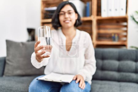 Photo for Young latin woman having psychology session offering water at psychology center - Royalty Free Image