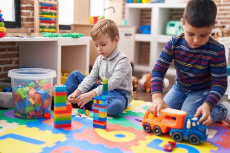 Téléchargez les photos : Deux enfants jouant avec des blocs de construction et camion jouet assis sur le sol à la maternelle - en image libre de droit