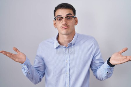 Photo for Handsome hispanic man wearing business clothes and glasses clueless and confused expression with arms and hands raised. doubt concept. - Royalty Free Image