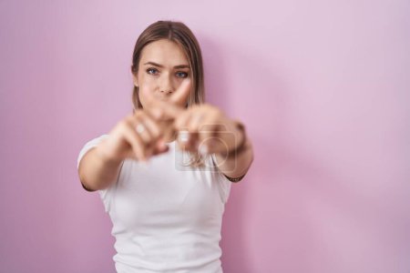 Téléchargez les photos : Blonde caucasian woman standing over pink background rejection expression crossing fingers doing negative sign - en image libre de droit