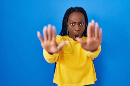 Photo for Beautiful black woman standing over blue background doing stop gesture with hands palms, angry and frustration expression - Royalty Free Image