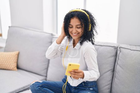 Téléchargez les photos : Jeune femme hispanique écoutant de la musique assise sur le canapé à la maison - en image libre de droit