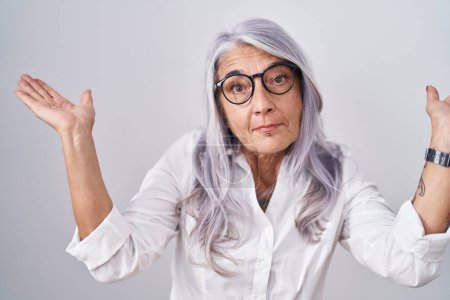 Photo for Middle age woman with tattoos wearing glasses standing over white background clueless and confused expression with arms and hands raised. doubt concept. - Royalty Free Image