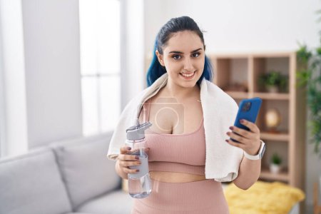 Téléchargez les photos : Young caucasian woman smiling confident holding water using smartphone at home - en image libre de droit