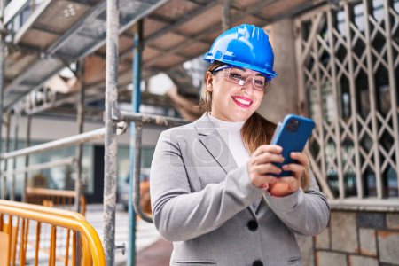Photo for Young beautiful hispanic woman architect smiling confident using smartphone at street - Royalty Free Image