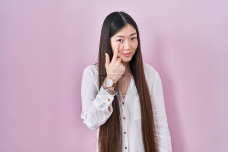 Téléchargez les photos : Chinese young woman standing over pink background pointing to the eye watching you gesture, suspicious expression - en image libre de droit
