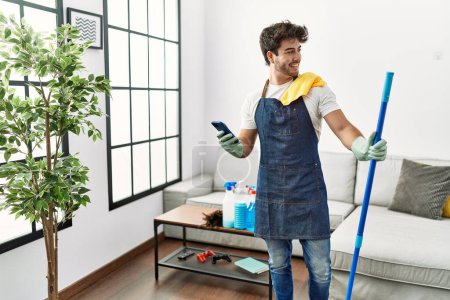 Photo for Young hispanic man smiling confident cleaning and using smartphone at home - Royalty Free Image