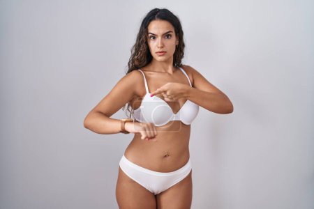 Téléchargez les photos : Young hispanic woman wearing white lingerie in hurry pointing to watch time, impatience, upset and angry for deadline delay - en image libre de droit