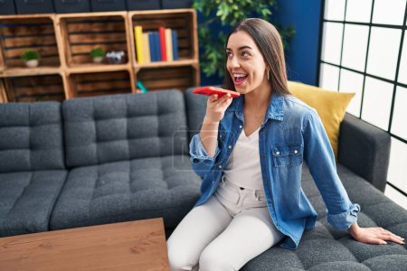 Téléchargez les photos : Jeune belle femme hispanique parlant sur smartphone assis sur le canapé à la maison - en image libre de droit