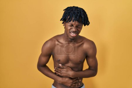 Foto de Hombre africano joven con rastas de pie sin camisa con la mano en el estómago porque la indigestión, la enfermedad dolorosa sensación de malestar. concepto ache. - Imagen libre de derechos