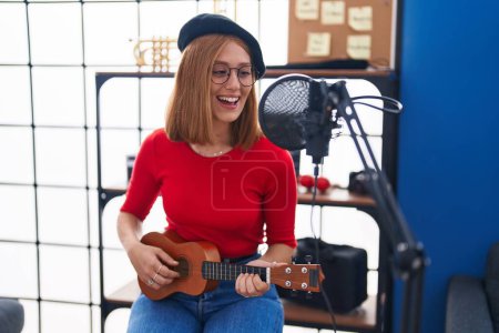 Téléchargez les photos : Jeune rousse femme musicienne chantant chanson jouant ukulele au studio de musique - en image libre de droit