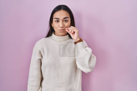 Foto de Young south asian woman standing over pink background mouth and lips shut as zip with fingers. secret and silent, taboo talking - Imagen libre de derechos