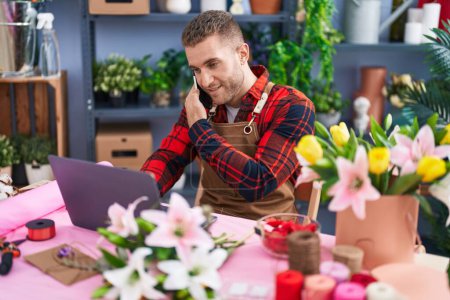 Téléchargez les photos : Young caucasian man florist talking on smartphone using laptop at flower shop - en image libre de droit