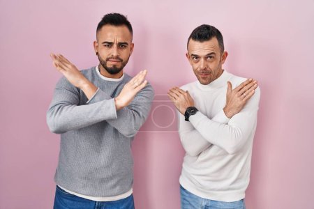Téléchargez les photos : Couple homosexuel debout sur fond rose expression de rejet croisant les bras faisant signe négatif, visage en colère - en image libre de droit