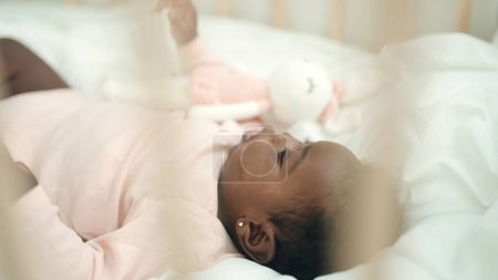 Téléchargez les photos : Bébé afro-américain couché sur le berceau avec une expression détendue dans la chambre - en image libre de droit