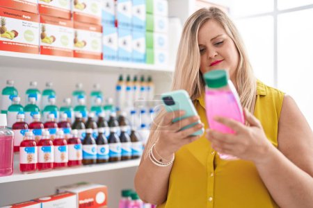 Photo for Young woman customer using smartphone holding shampoo at pharmacy - Royalty Free Image