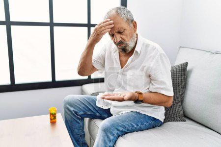 Foto de Hombre mayor de cabello gris tomando píldora para el dolor de cabeza en casa - Imagen libre de derechos