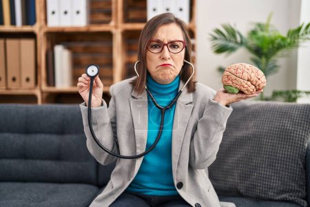Foto de Middle age hispanic woman working at therapy office holding brain depressed and worry for distress, crying angry and afraid. sad expression. - Imagen libre de derechos