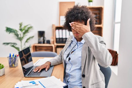 Téléchargez les photos : Black woman with curly hair wearing call center agent headset at the office covering eyes with hand, looking serious and sad. sightless, hiding and rejection concept - en image libre de droit