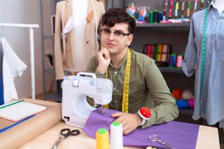 Photo for Non binary man tailor smiling confident sitting on table at atelier - Royalty Free Image