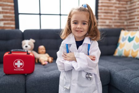 Photo for Adorable hispanic girl wearing doctor uniform standing with arms crossed gesture at home - Royalty Free Image