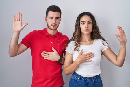 Photo for Young hispanic couple standing over isolated background swearing with hand on chest and open palm, making a loyalty promise oath - Royalty Free Image