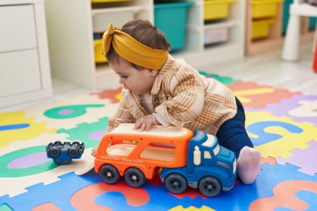 Foto de Adorable niño rubio sentado en el suelo jugando con el camión en el jardín de infantes - Imagen libre de derechos