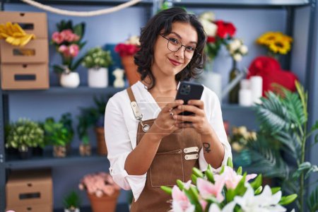 Photo for Young beautiful hispanic woman florist smiling confident using smartphone at flower shop - Royalty Free Image